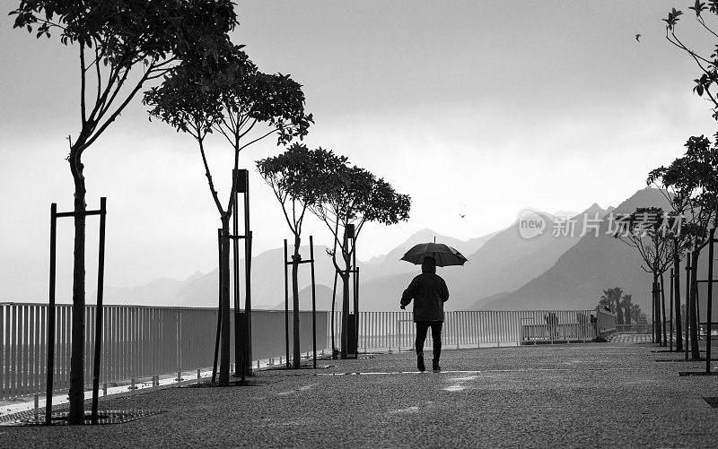 成熟的男人撑着伞走在雨中的城市街道上