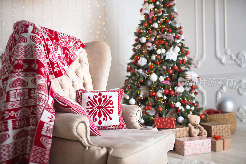 在白色的客厅里，一棵红色和白色装饰的圣诞树下，礼物在盒子里特写。新的一年,