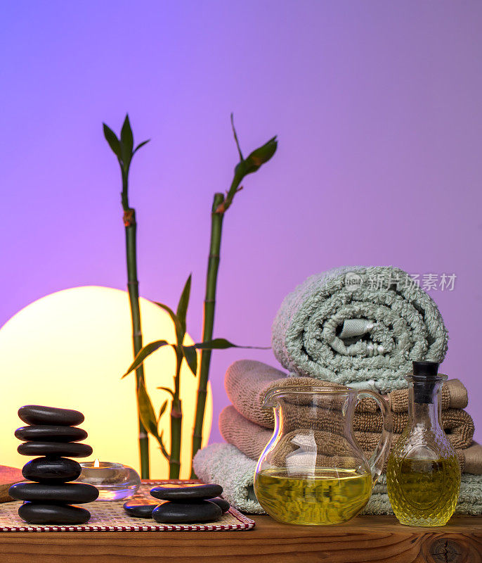 美丽水疗概念-黑色按摩石，竹植物，蜡烛，毛巾和油在木桌子上日落