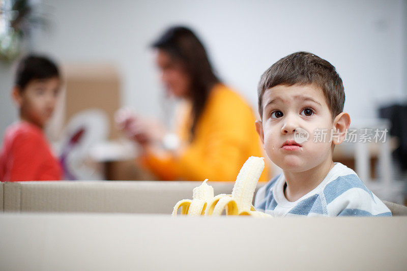 蹒跚学步的孩子在移动的箱子里吃着两根香蕉，他的嘴是凌乱的