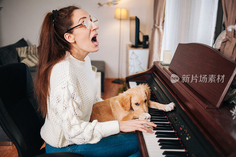 一个女人在练钢琴和唱歌，她的狗躺在她的腿上