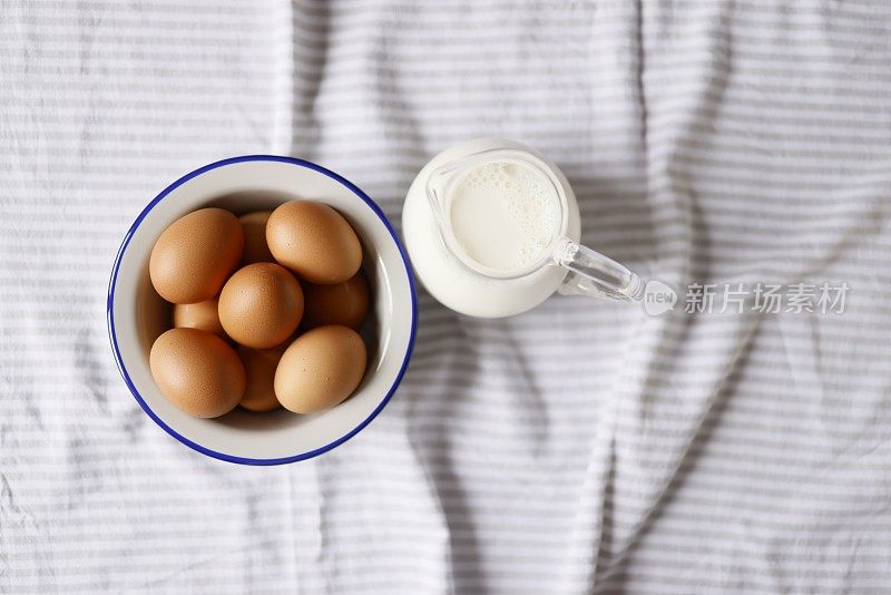 一盘棕色鸡蛋上有灰白色条纹盖，盘灰搪瓷，侧面涂海军蓝。盘子旁边的玻璃罐里有牛奶