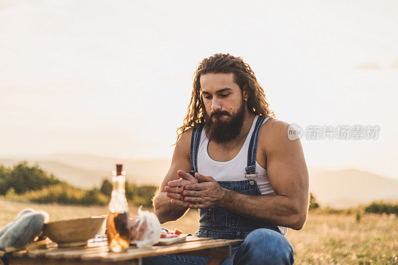 自然的守护者。一个在山上的男人，一个伐木工人，喝着自制的白兰地，吃着自制的食物，而在他身后是美丽的日落，休息辛苦的工作。