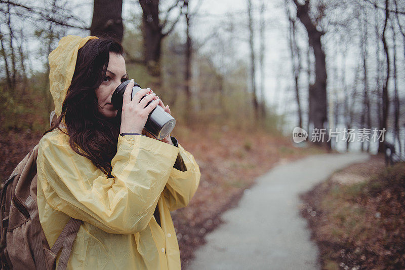 一个快乐的年轻女子在一个下雨天穿着一件黄色雨衣在树林里享受大自然。