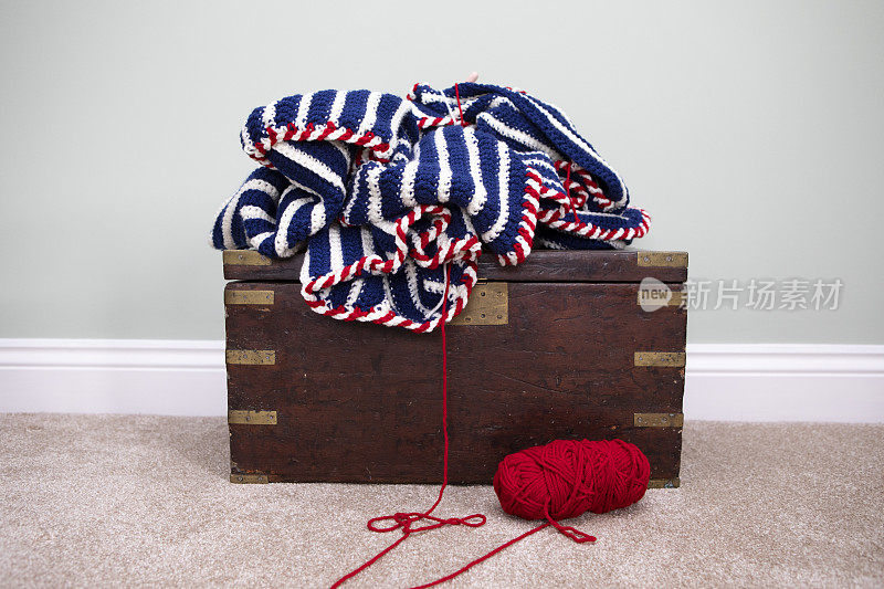 钩织毯子和红色羊毛球放在一个古董箱子上的地毯地板上的家庭房间