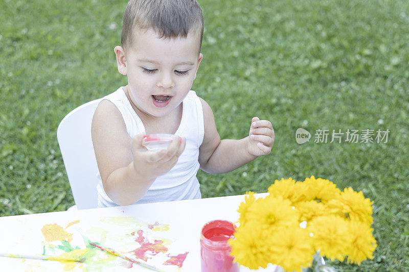 一个可爱的小男孩用画笔画画。绘画的乐趣。一个小男孩在家里的花园里画画。
