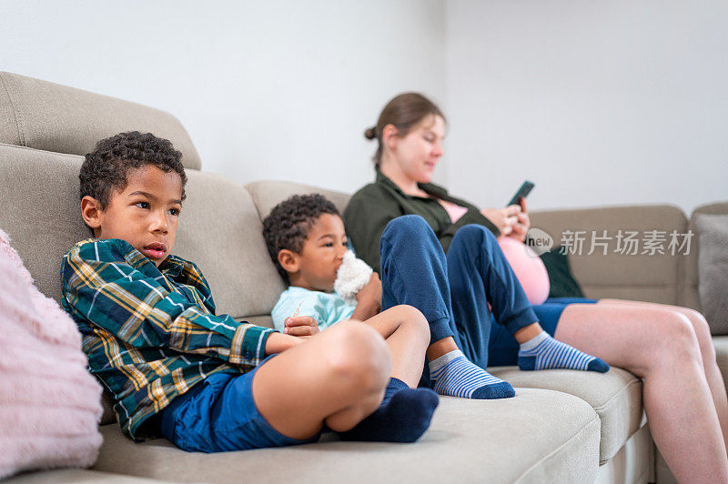 一个成年孕妇和两个小男孩坐在客厅的沙发上