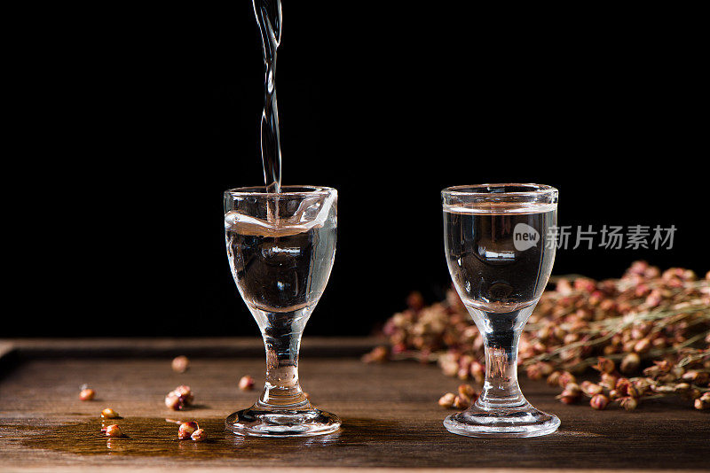 在木头背景上，中国白酒从瓶子里倒进玻璃杯里
