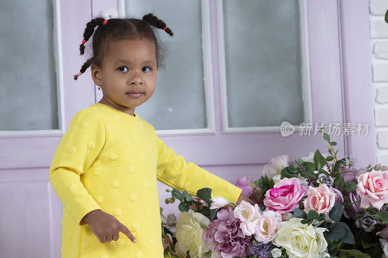 身穿黄色连衣裙的非洲裔美国小女孩用手触摸一束鲜花。