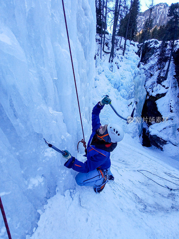 一个年轻人在冰冻的瀑布上攀冰，他使用冰镐