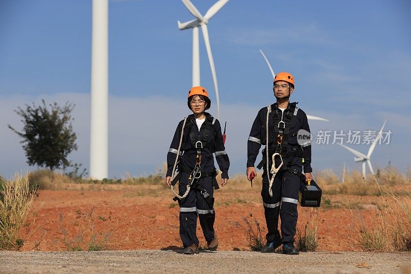 男、女工程师同事扛着工具和设备箱走在风力发电机组，可再生和绿色能源的概念