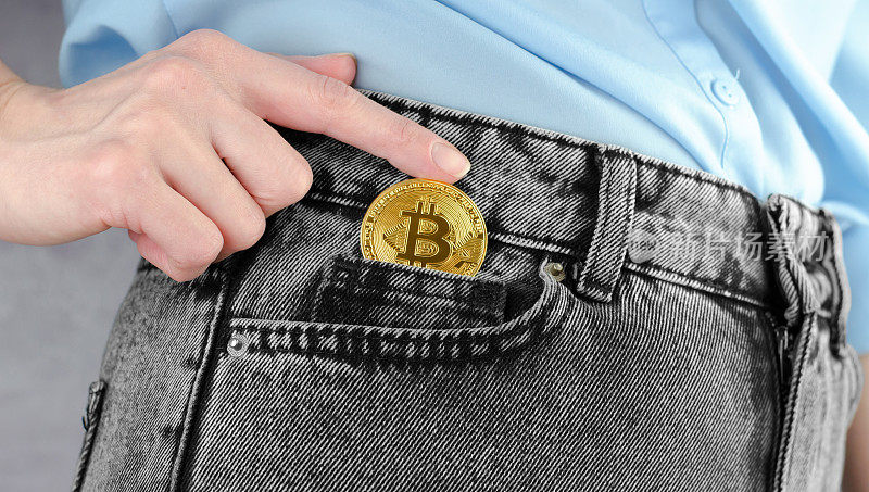 黄金比特币币在女性手中的特写。一个女人的手把黄金比特币放进她的牛仔裤口袋里。Cryptocurrency。