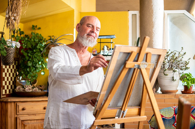 一个自信快乐的老人享受着他的空闲时间和生活，在他的客厅里画画。