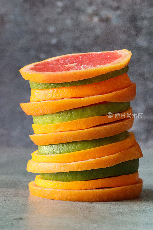 特写图像交替切片柑橘水果堆，粉色葡萄柚，酸橙和橙片，斑驳的灰色背景，重点在前景