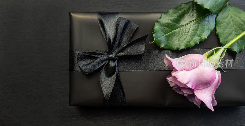 礼品盒用黑色的纸包装，黑色的背景上有一个黑色的蝴蝶结。玫瑰。节日的概念。“黑色星期五”。