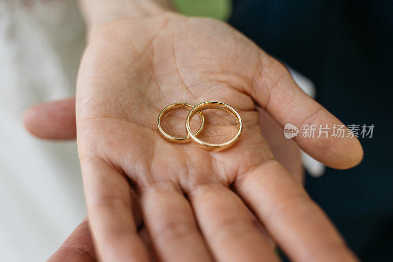 两个结婚戒指的特写放在新娘和新郎的手上