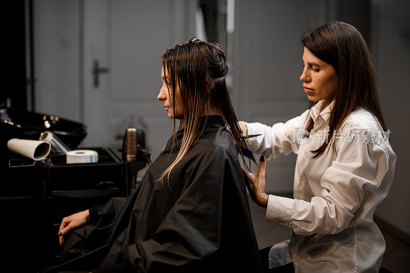 美发师在美容院熟练地用剪刀为女顾客理发。