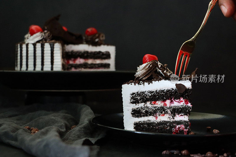 黑色森林大门切片的图片，上面有莫雷罗樱桃，叉子插入豪华巧克力蛋糕，上面有奶油和融化的巧克力，黑色背景，三层