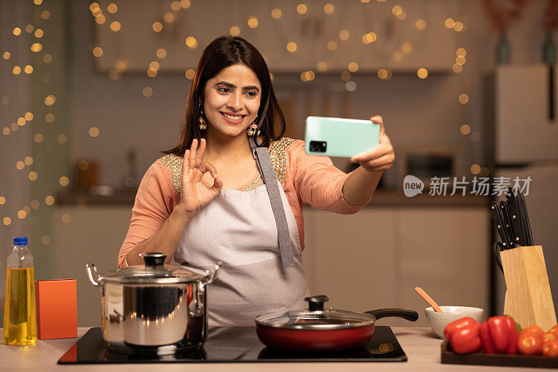 微笑的年轻印度女子在家里厨房做饭时用智能手机自拍的照片
