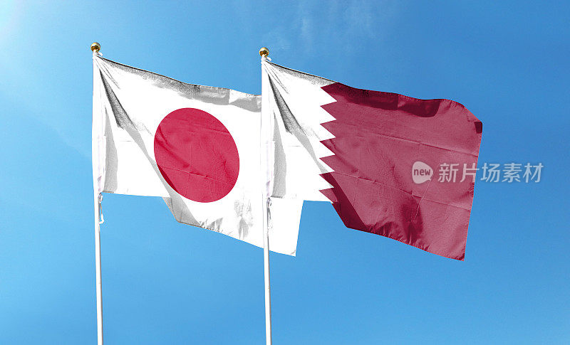 多云天空上的日本国旗和卡塔尔国旗。在天空中摇曳