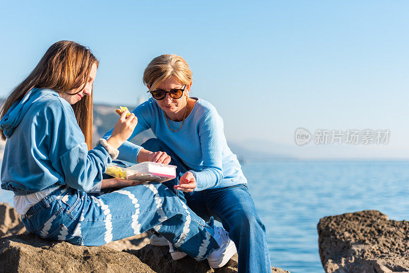 阳光明媚的冬日，母亲和十几岁的女儿在岩石海滩上野餐的快乐时刻