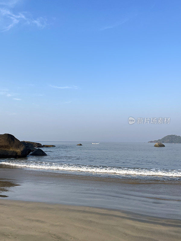 印度果阿邦Palolem海滩的海岸线，海浪拍打着海滩，船在地平线上，湛蓝晴朗的天空