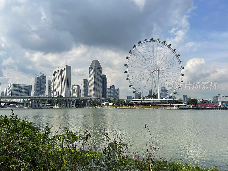 新加坡摩天轮的图像，阳光明媚，多云的蓝天为背景，城市海滨景观，摩天大楼，重点在前景