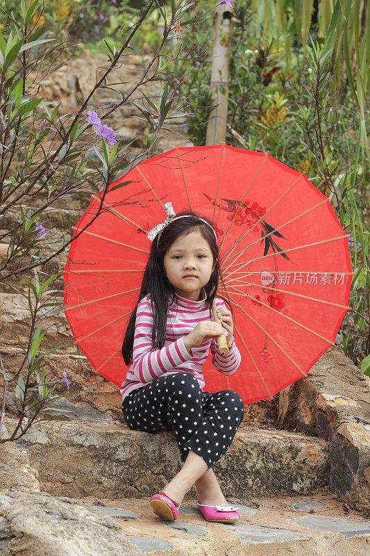一个可爱的小女孩在公园里撑着一把红色的伞