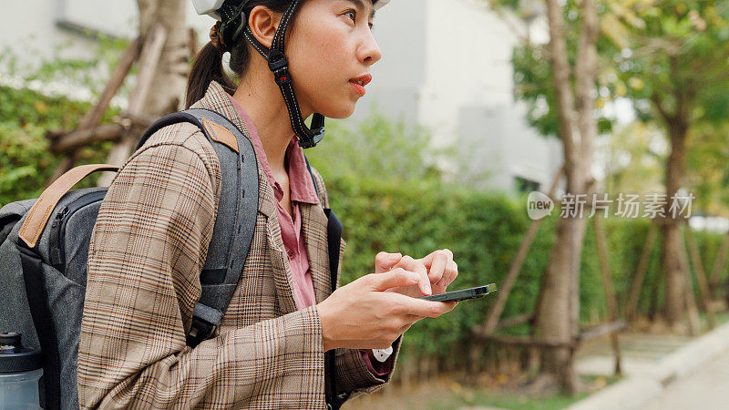 年轻的亚洲女商人使用智能手机和自行车从家里去办公室上班。业务通勤。