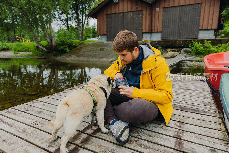 挪威，一名身穿黄色夹克的男子在湖边与一只狗玩耍