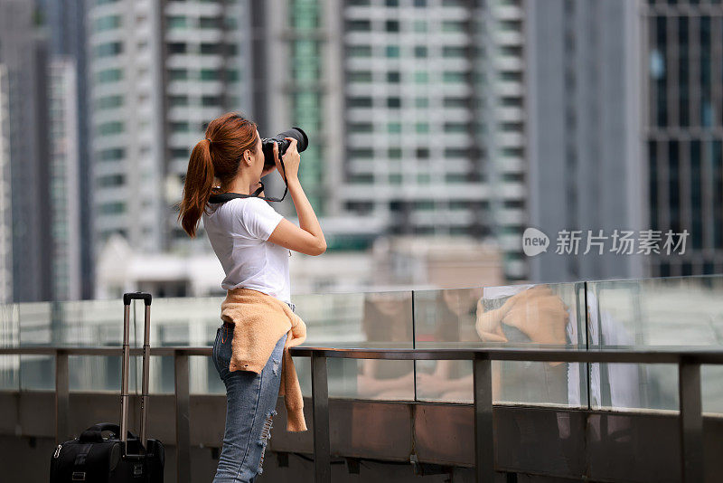 亚洲女性游客或学生在城市街道上用数码相机拍照的肖像。度假旅游概念。一名年轻女子在高楼上拍摄曼谷城市的照片。旅游及旅游概念