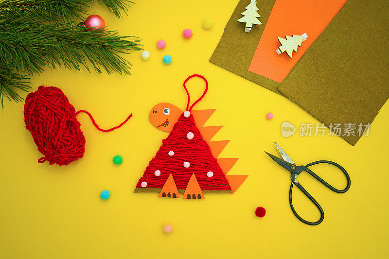 一个孩子用硬纸板和红线做成的圣诞树玩具恐龙躺在黄色的背景上。2024年的象征。教育和手工艺活动。