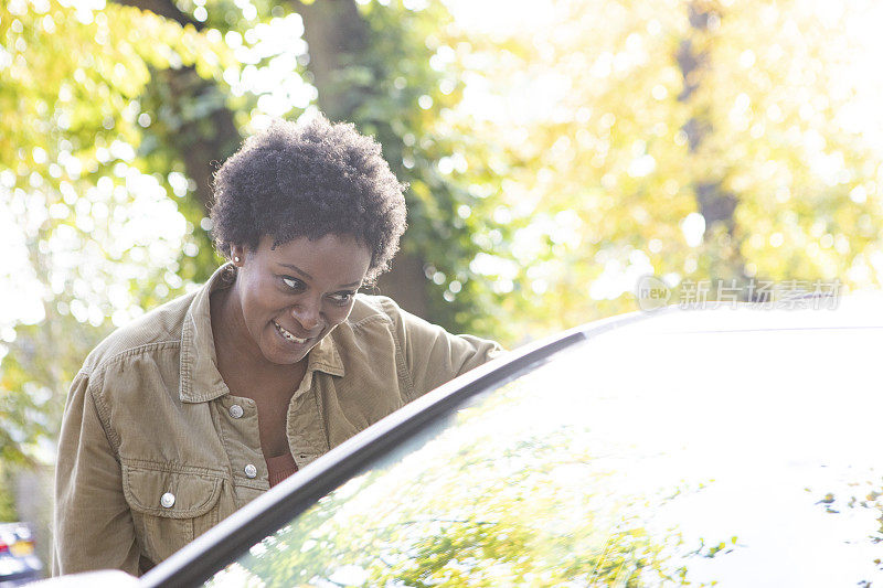 一个微笑的女人站在一辆停在住宅区街道上的汽车旁
