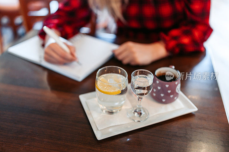 年轻女子一边喝咖啡，一边在咖啡馆里写笔记本
