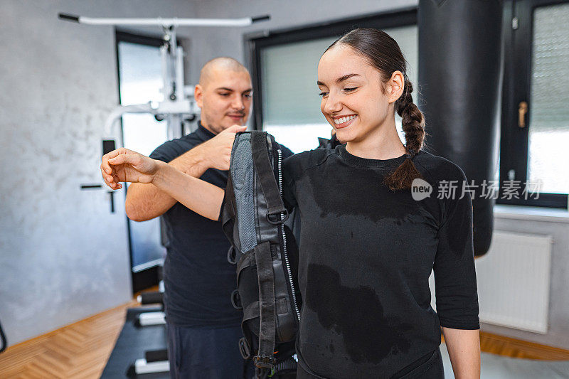 私人教练帮助他的女客户在健身工作室穿着EMS西装