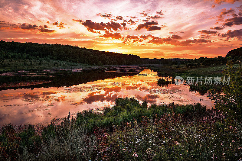 一个宁静的日落在一个宁静的湖，与橙色和红色的充满活力的色调反映在平静的水。田园诗般的场景。