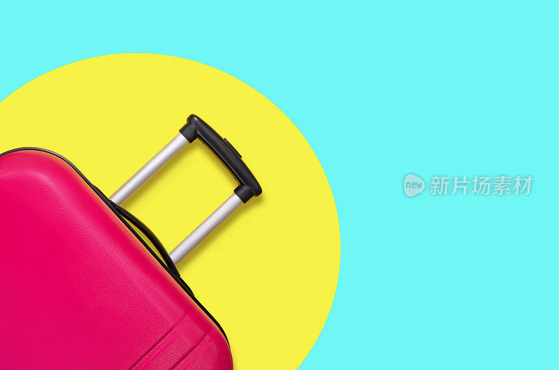 黄色和蓝色背景上的粉色行李箱。旅行的概念。