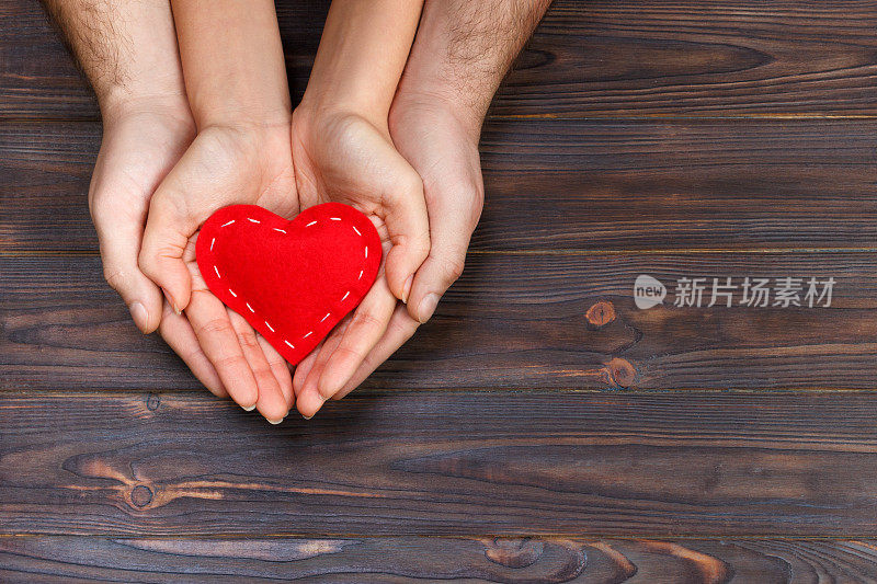 爱情、家庭的概念。近距离的男人和女人的手握着红色的橡胶心在一起