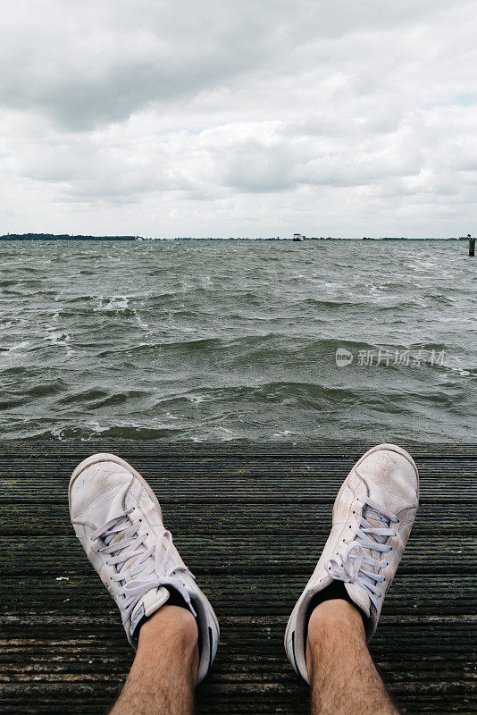 一个人坐在码头上，前景是运动鞋，背景是海景