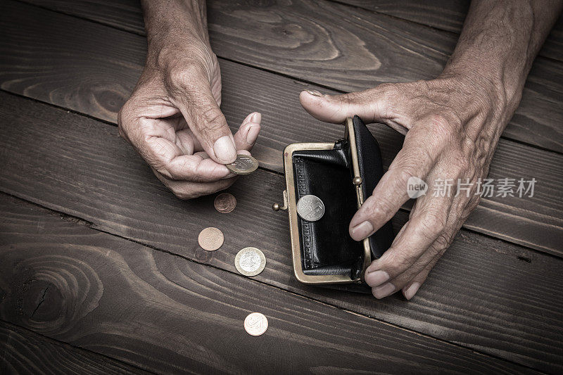 一个老人把硬币放在空空的旧皮夹上。退休后贫困的概念。