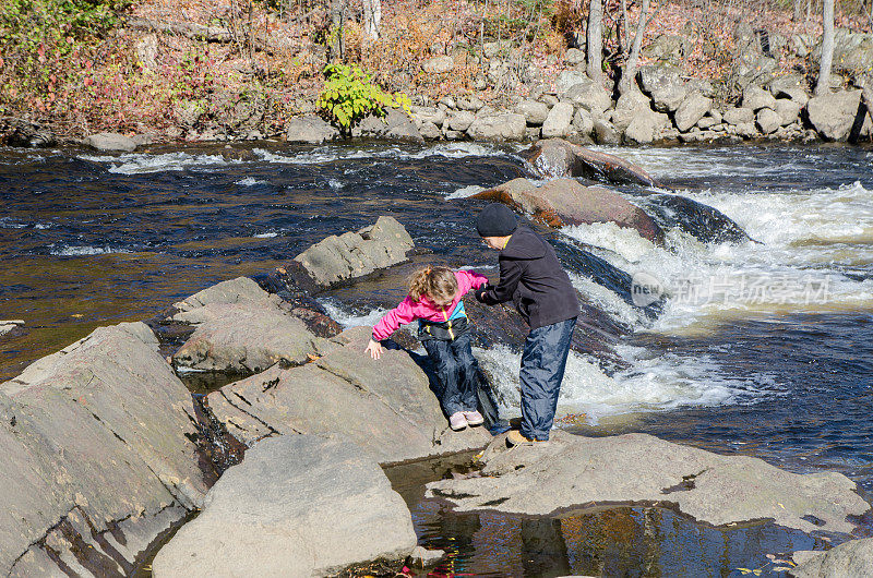 秋天的一天，魁北克市，一个男孩帮助他的妹妹在圣查尔斯河上的岩石上行走
