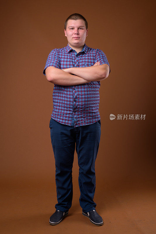 摄影棚里的超重年轻男子穿着紫色格子衬衫，背景是彩色的