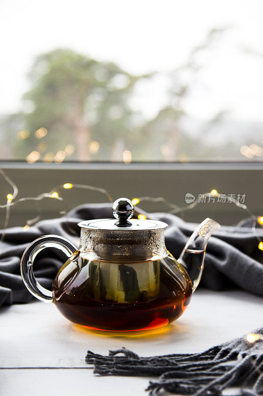 一个放着红茶的茶壶，旁边有一条灰色的围巾和一个圣诞花环。冬天的概念