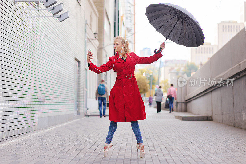 女芭蕾舞演员在城市里拿着智能手机和雨伞