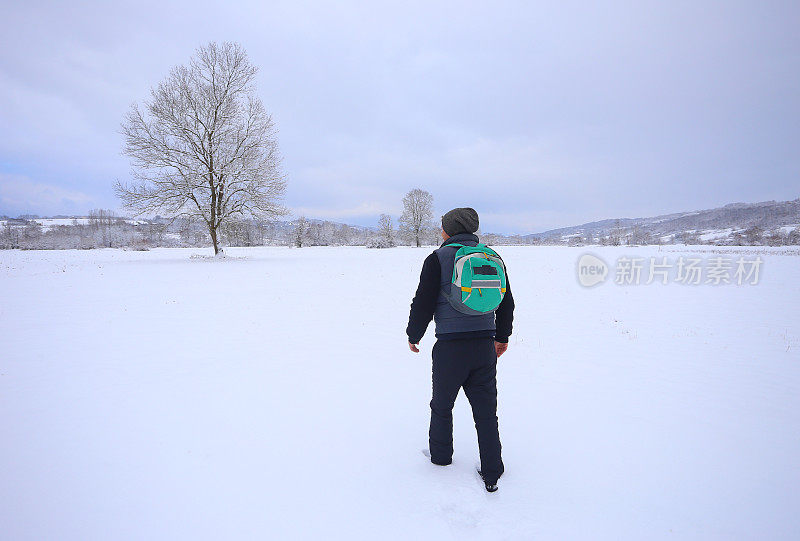 英俊的成年男子徒步旅行者戴着针织帽徒步在下雪的冬天的自然