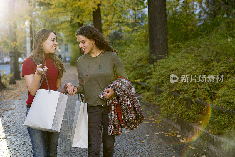 购物:两个年轻的女人拿着购物袋走在街上