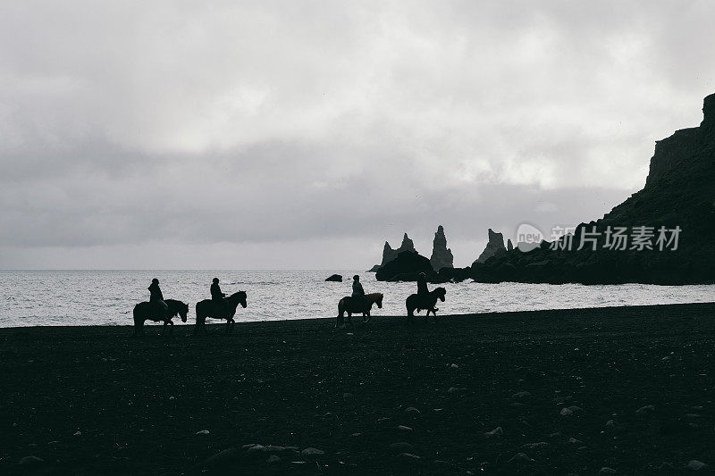 冰岛维克黑沙滩上骑着马的人的剪影