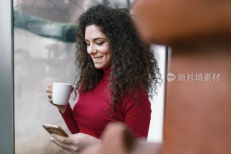漂亮的年轻女子一边喝咖啡一边玩智能手机