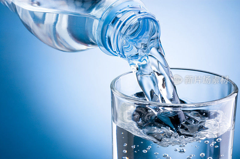 将水从瓶子倒入蓝色背景的玻璃杯中