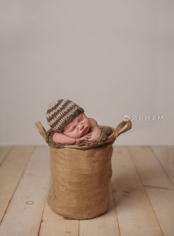新生儿戴着针织帽，睡在土豆袋里